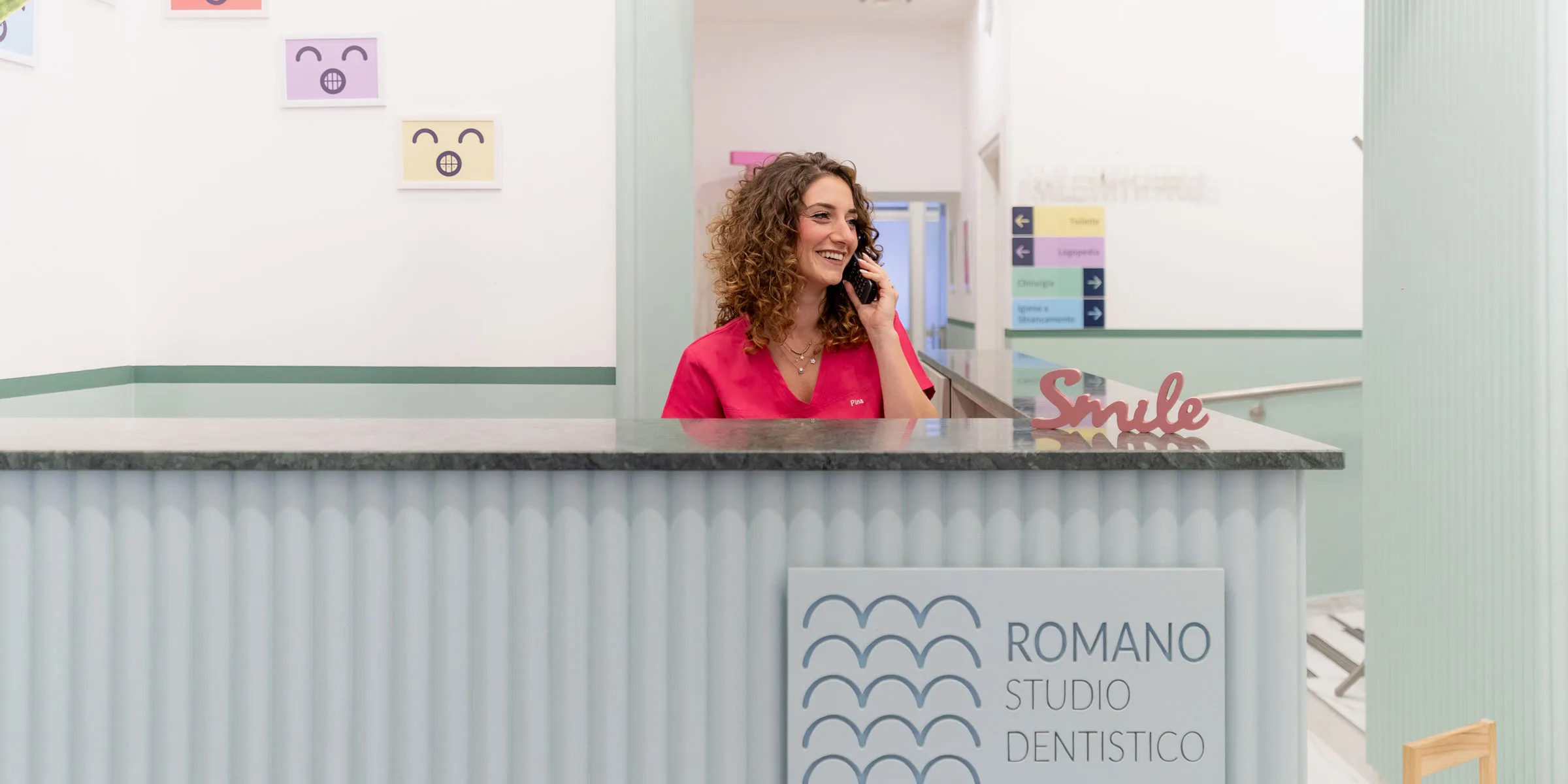 Reception dello Studio Dentistico Romano con la segreteria al telefono e la scritta Smile sul bancone